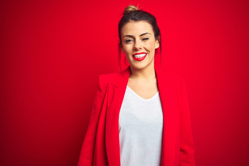 Young beautiful business woman standing over red isolated background winking looking at the camera...