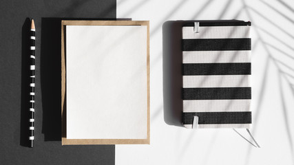 Black and white striped notebook and white blanket with a black and white striped pencil  on a black and white background with a leaf shadow
