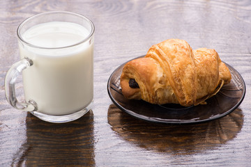 croissant on a brown plate next to a mug of milk on a wooden background