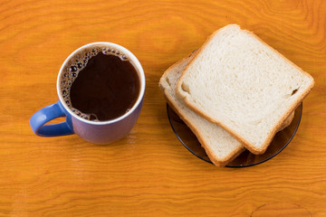 bread on a brown plate next to strawberry jam and with a mug of milk on a wooden background