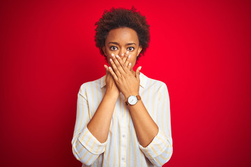 Fototapeta na wymiar Young beautiful african american woman with afro hair over isolated red background shocked covering mouth with hands for mistake. Secret concept.