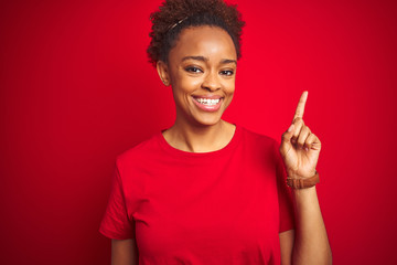 Young beautiful african american woman with afro hair over isolated red background with a big smile on face, pointing with hand finger to the side looking at the camera.