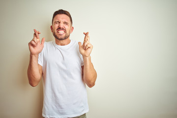 Young handsome man wearing casual white t-shirt over isolated background gesturing finger crossed smiling with hope and eyes closed. Luck and superstitious concept.