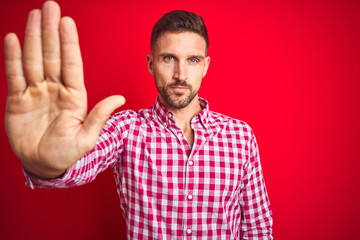 Young handsome man over red isolated background doing stop sing with palm of the hand. Warning expression with negative and serious gesture on the face.