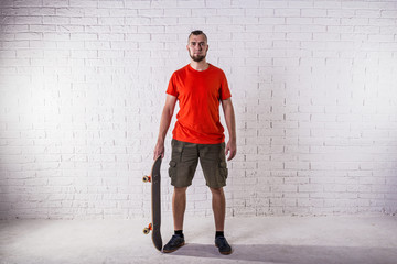 Skateboarder standing with skateboard on the background of a white wall.