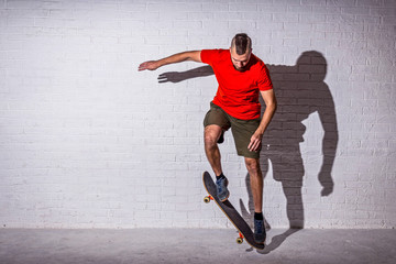Skateboarder jumping ollie on a skateboard on the background of a white wall.