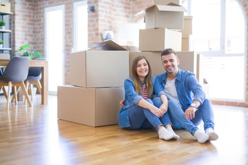 Young beautiful couple in love moving to new home, sitting on the floor very happy and cheerful for new apartment around cardboard boxes