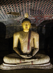 The traditional Sri Lankan image of the Buddha meditation in the Lotus position, with a fiery ushnisha on his head, embodied in stone. Visible elements of ancient frescoes, in cave temple in Dambulla.