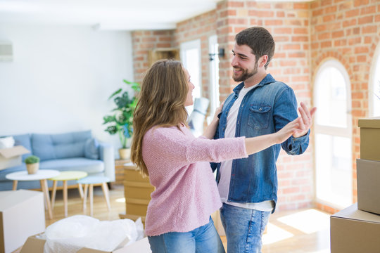 Young couple dancing celebrating moving to new apartment around cardboard boxes