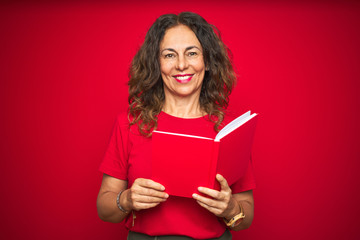 Middle age senior woman reading a book over red isolated background with a happy face standing and...