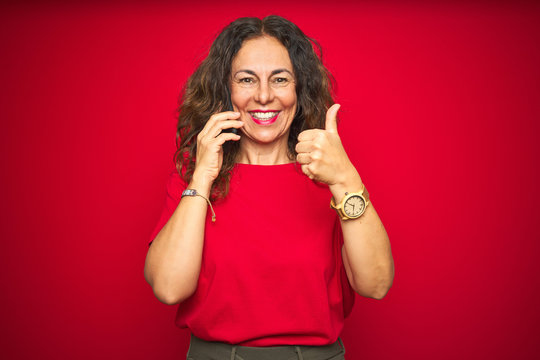 Middle Age Senior Woman Talking On The Phone Over Red Isolated Background Happy With Big Smile Doing Ok Sign, Thumb Up With Fingers, Excellent Sign