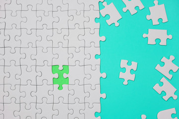 Fragment of a folded white jigsaw puzzle and a pile of uncombed puzzle elements against the background of a yellow surface.