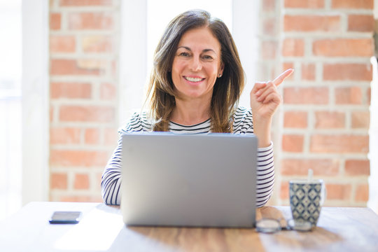 Middle age senior woman sitting at the table at home working using computer laptop very happy pointing with hand and finger to the side
