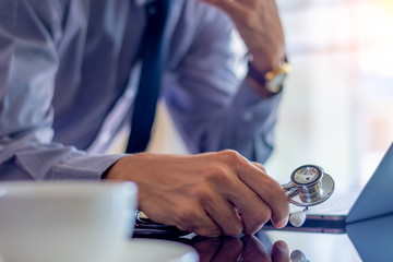 Smart male doctor standing and working on laptop computer at office in clinic or hospital.