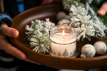 Winter cozy home deco rustic concept with woman holding wooden tray with fir tree branches and candle, cozy home concept