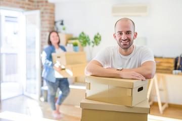 Naklejka na ściany i meble Young couple moving to new apartment, handsome man leaning on cardboard boxes and smiling happy