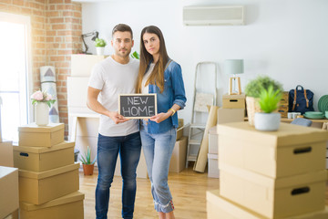 Young beautiful couple holding blackboard with new home text at new house with a confident...