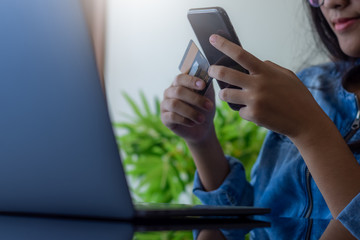 Young asian smiling woman hand holding credit card and using mobile smart phone for online shopping and payment at home.  