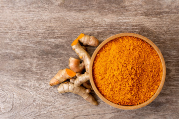 Turmeric powder in wooden bowl and tumeric root isolated on rustic wood table background. Top view.  