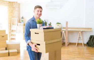 Fototapeta na wymiar Handsome young man smiling happy moving to a new home, very excited holding cardboard boxes at new apartment