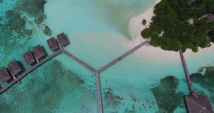 4K Aerial drone view of a luxury island resort on exotic white sand beach and over-water villas in Maldives. Blue lagoon and palm trees. Travel agency and trip advisor concept
