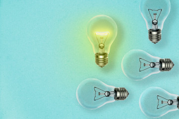 Idea concept background with many lightbulbs and one lit on a blue paper sheet and copy space for your text