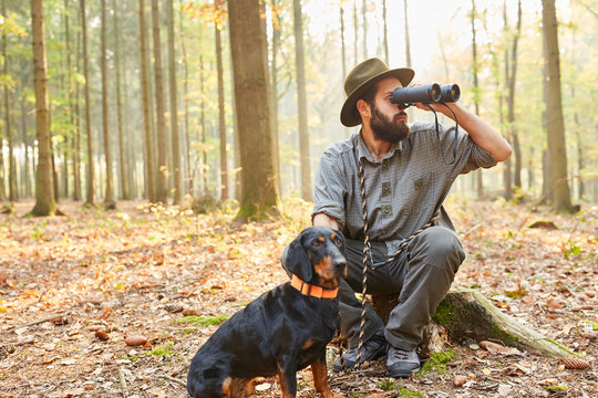 Revierf&ouml;rster mit Jagdhund schaut durch Feldstecher