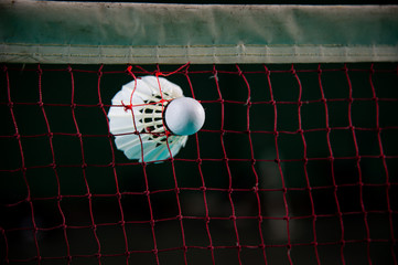 Closeup white Badminton shuttlecock hang on red net with blurred background.