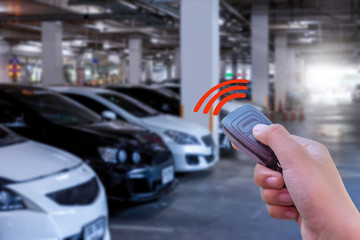 Closeup man hand holding and using remote control to lock or unlock the car with car parking...