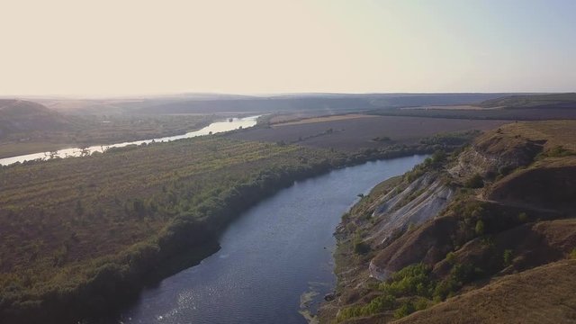 Top view of Dnestr (Dniester) river in autumn. River surrounds yellow field and green forest. Moldova republic of.