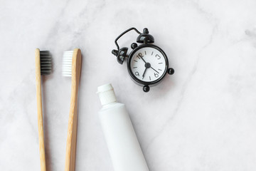 Set of eco-friendly toothbrushes, toothpaste, clock on marble background. Dental and healthcare concept. Top view, flat lay.