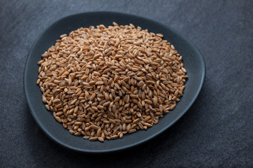 uncooked spelt on black dish on ceramic background