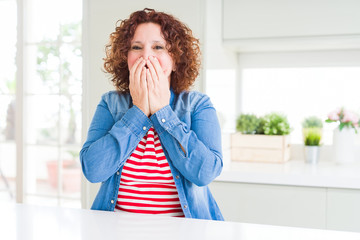 Middle age senior woman with curly hair wearing denim jacket at home laughing and embarrassed...