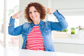 Middle age senior woman with curly hair wearing denim jacket at home smiling pointing to head with both hands finger, great idea or thought, good memory