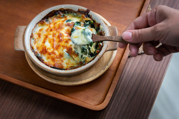 Use a spoon to scoop the delicious baked spinach, appetizing cheese, served in a bowl on a wooden table