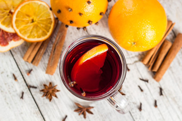 Glass of delicious mulled wine with oranges anise cinnamon on white wooden table