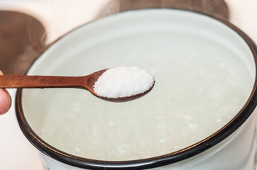 Fototapeta na wymiar Add salt from a wooden spoon to boiling water.