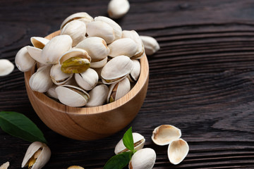  Pistachio in wooden bowl in background with green leaves.