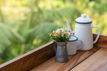 The flower vase has white-yellow flowers placed beside the teapot on the wooden floor.