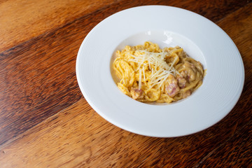 Delicious spaghetti, bacon topped with cheese, served on a white plate on brown wooden table top