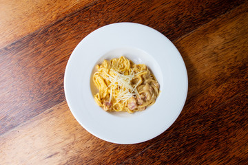 Delicious spaghetti, bacon topped with cheese, served on a white plate on brown wooden table top