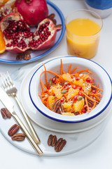 Healthy raw vegetarian salad with carrot, pomegranate seeds, oranges, pumpkin seeds, pecan nuts. Glass of orange juice and pomegranate on the background.