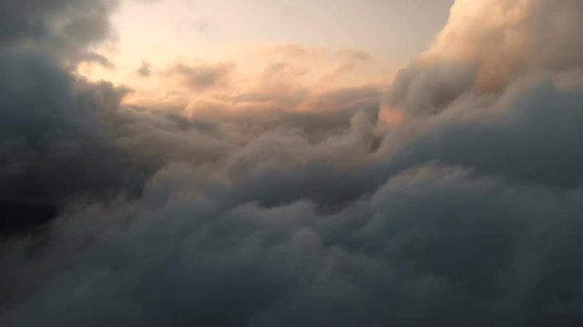 Aerial view flying through cumulus thunderclouds at sunset. Gold colored sunset cloudiness in high contrast. Real sky. The concept of dreams and weather forecast