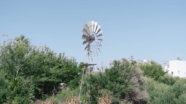 Old rusty wind powered water pump mill turning on clear windy day 