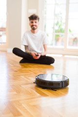 Young man using automatic vacuum cleaner to clean the floor, controling machine housework robot