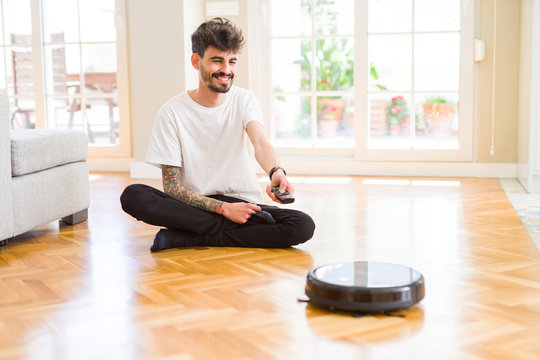 Young man using automatic vacuum cleaner to clean the floor, controling machine housework robot