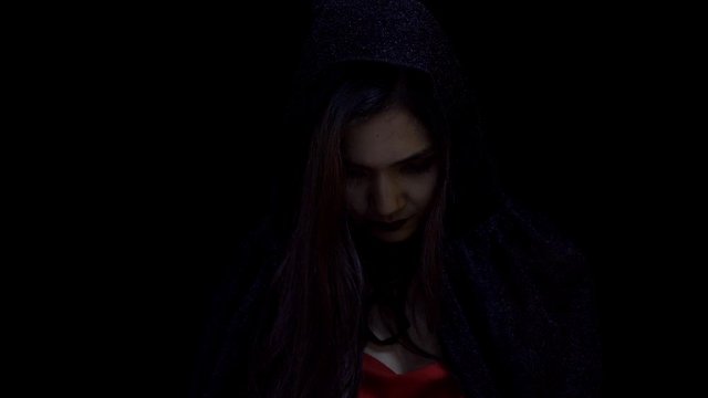 Asian woman in witch Halloween costume opening black head scarf and looking at camera, in slow motion 