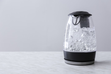 Transparent electric kettle with boiling water on table
