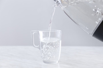 Pouring of boiled water from electric kettle into cup on table