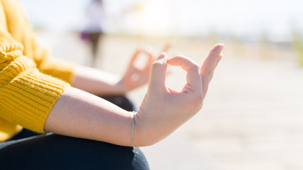 Beautiful young woman sitting on a promenade by the sea doing yoga pose, meditating enjoying sunlight and relaxing on sunny day